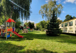 Ogród przedszkolny a w nim piękny, nowoczesny, kolorowy plac zabaw, z prawej strony budynek.